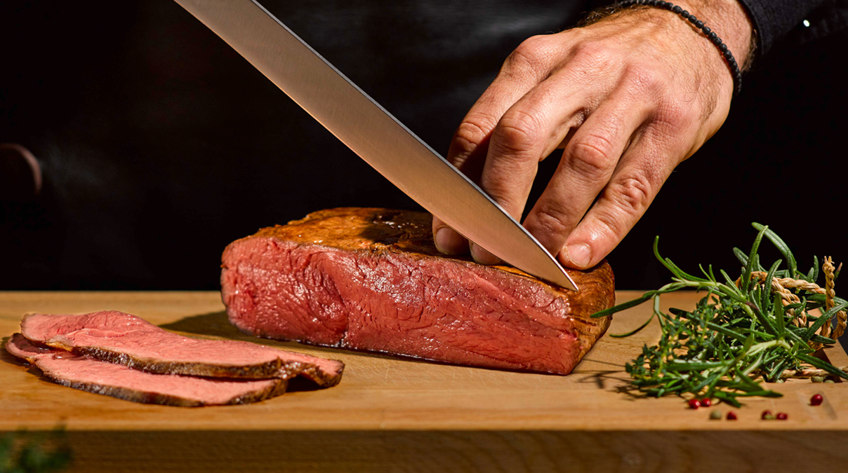 Koch schneidet Fleisch in Küche